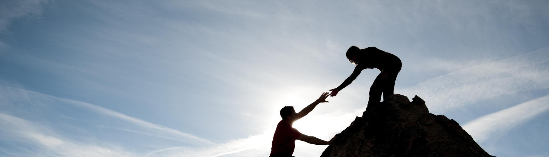Zwei Personen auf einem Felsvorsprung; eine hilft der anderen nach oben